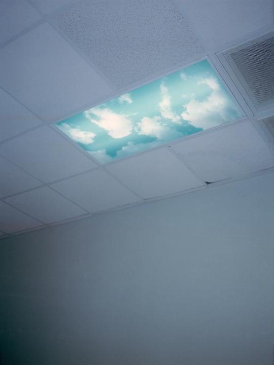A ceiling panel with a sky and clouds design is visible in a room with a plain wall.