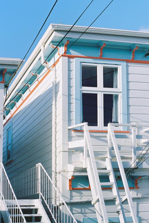 A white house with blue and orange trim is shown from a low angle, with white stairs leading up to a window.