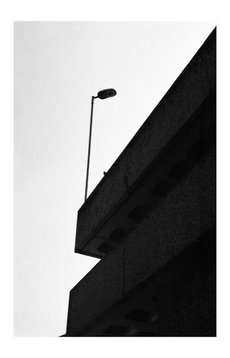 A street light stands tall against a bright sky, with a dark concrete building in the foreground.