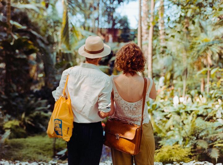 A couple walks away from the viewer through a lush indoor garden.