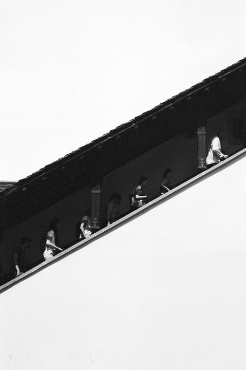 A group of people walk along a covered walkway on the side of a building.