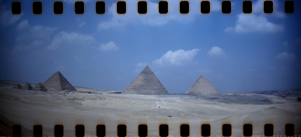 Three pyramids stand in a desert landscape under a blue sky with scattered clouds.