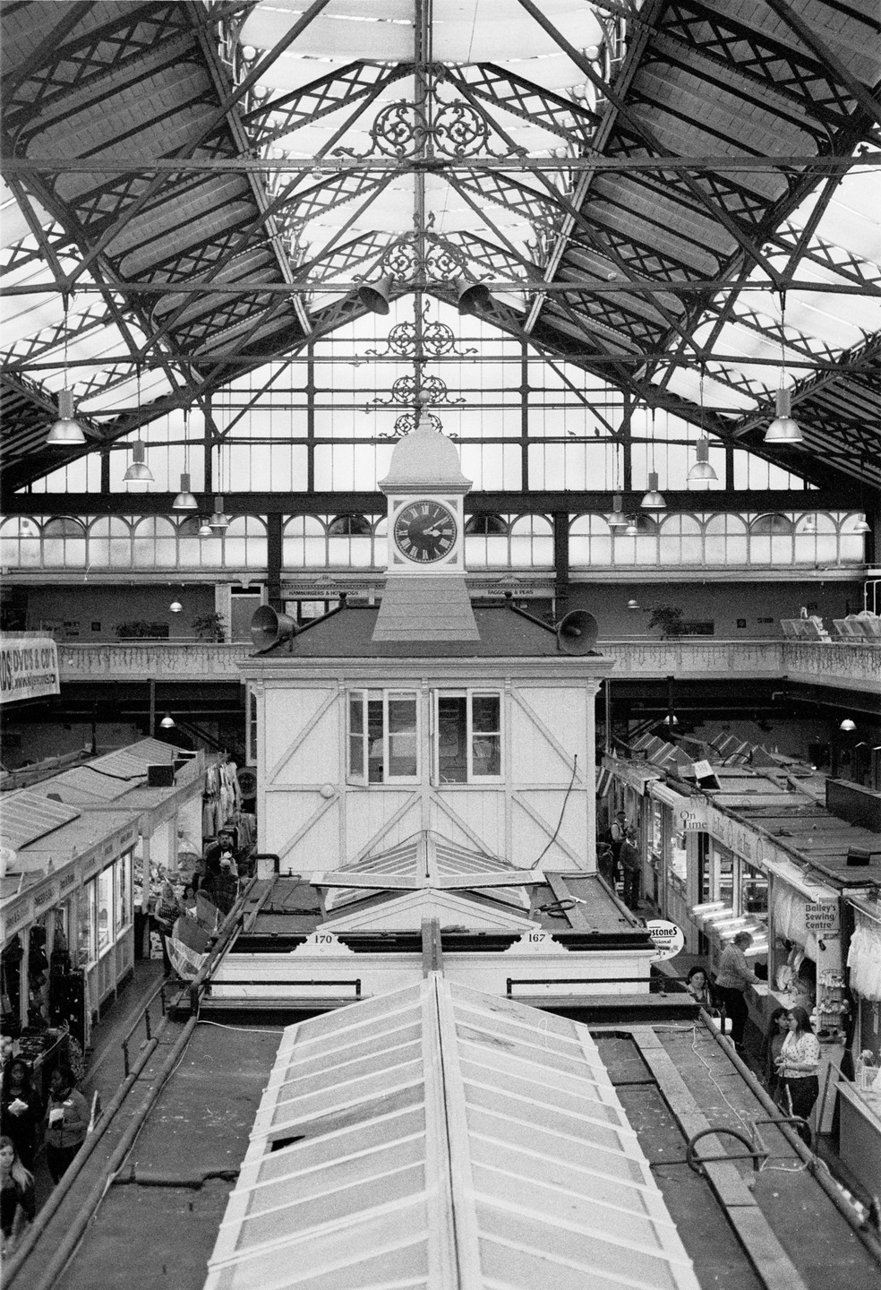 A clock tower stands in the middle of a market hall with a large glass and metal roof.
