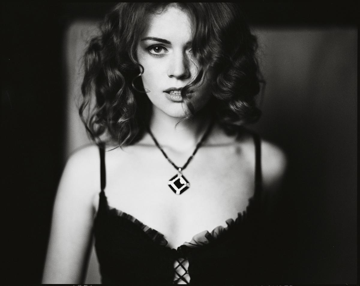 A woman with curly hair and a necklace looks directly at the viewer.