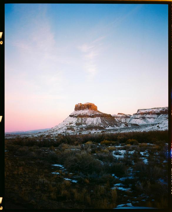A snow-dusted mesa stands under a pink and blue sky at dusk.