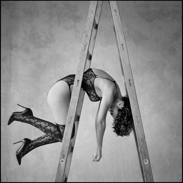 A woman in lingerie and high heels is draped over a wooden ladder.