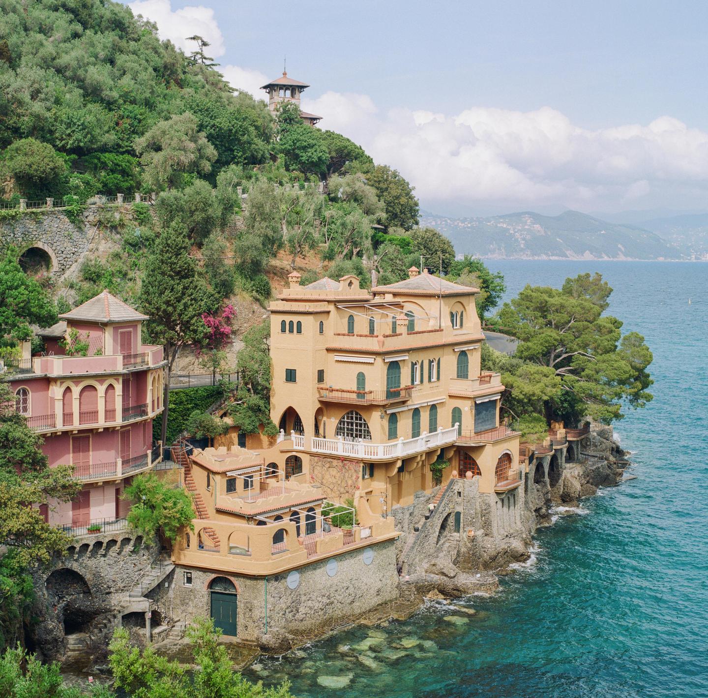A large villa with multiple balconies and terraces is built into a cliffside overlooking the sea.
