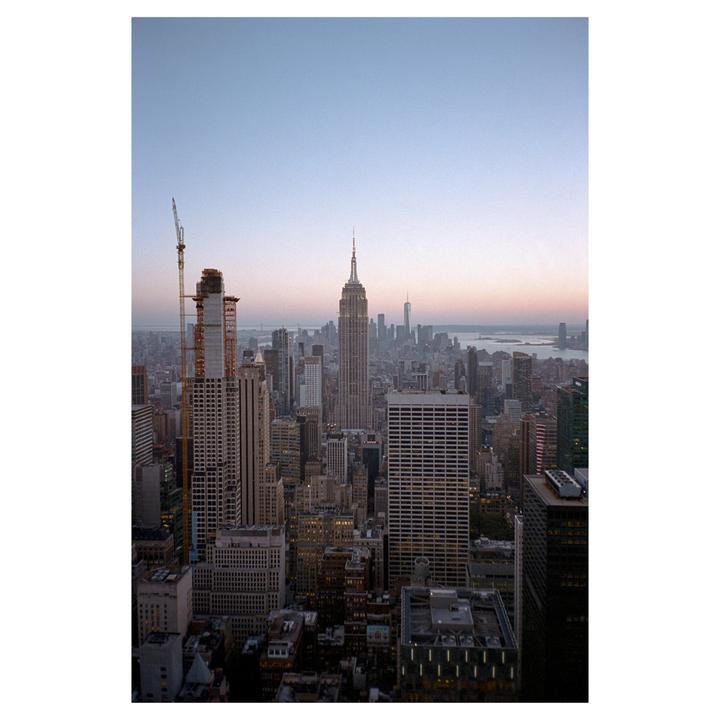 A panoramic view of the New York City skyline shows many buildings, including the Empire State Building, under a clear sky.