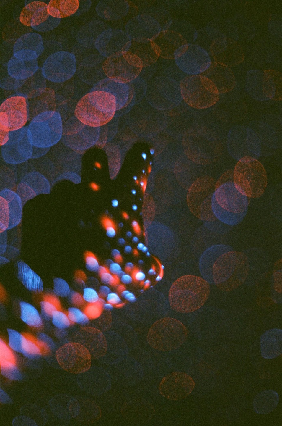 A hand is silhouetted against a background of red and blue bokeh lights.