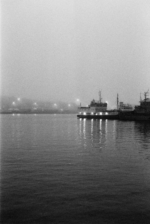 A boat with lights on is docked in a harbor on a foggy night.