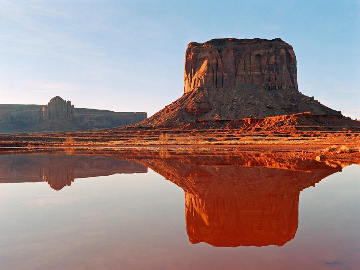 A large mesa is reflected in a body of water in Monument Valley.