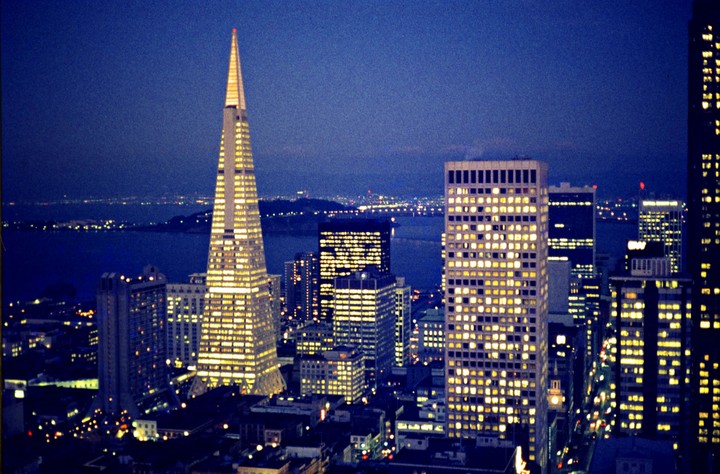 The Transamerica Pyramid and other buildings are illuminated at night with a body of water and city lights in the background.