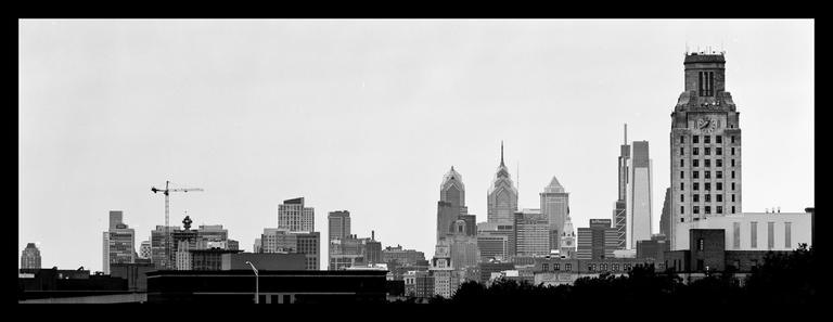 A panoramic black and white image shows a city skyline with a large clock tower and several skyscrapers.