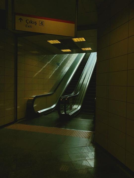 An exit sign hangs above two escalators in a subway station.