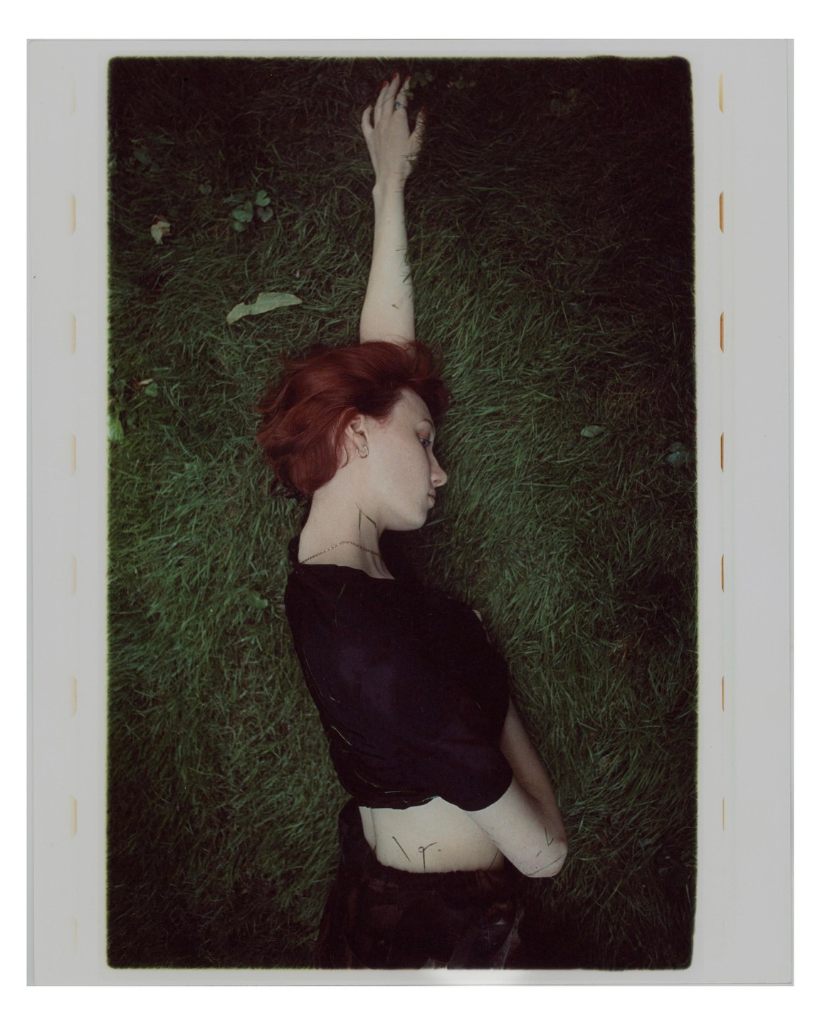 A woman with red hair lies on her back in green grass with one arm extended above her head.