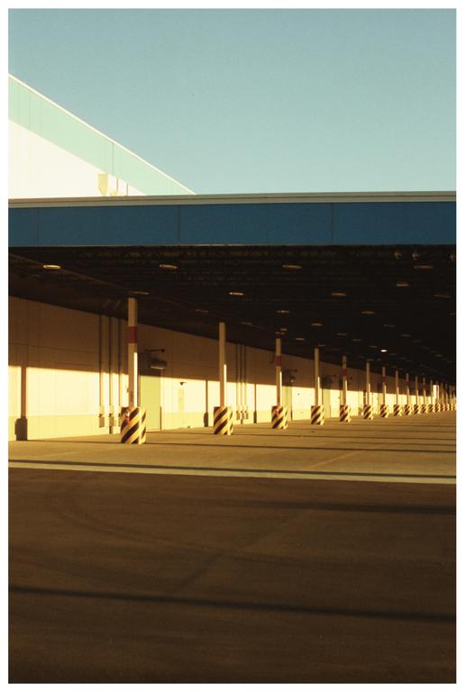 A long row of striped bollards stands in front of a building with a blue roof under a clear sky.