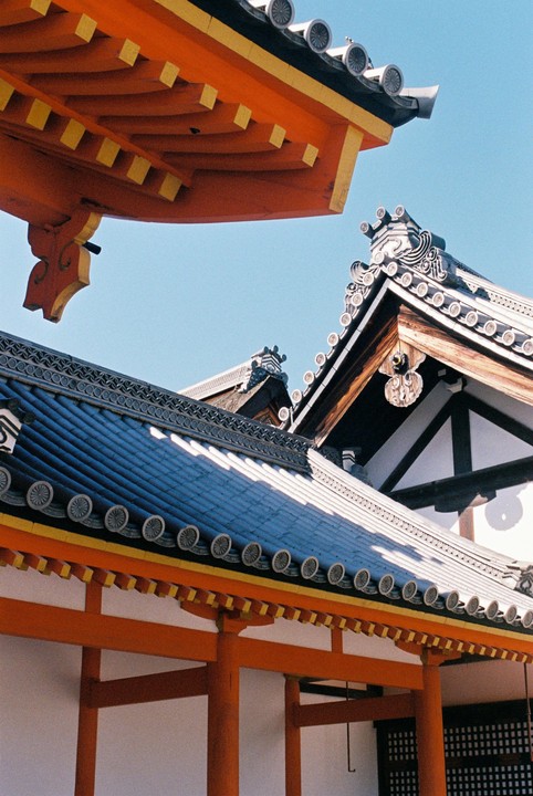 Three traditional Japanese roofs with ornate tiles and orange eaves are visible against a clear blue sky.