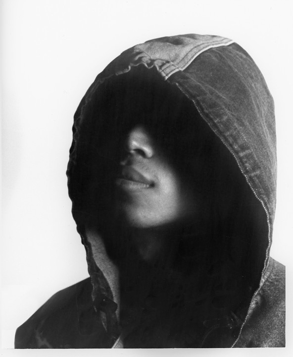 A person wearing a hooded jacket has their face obscured by shadow.