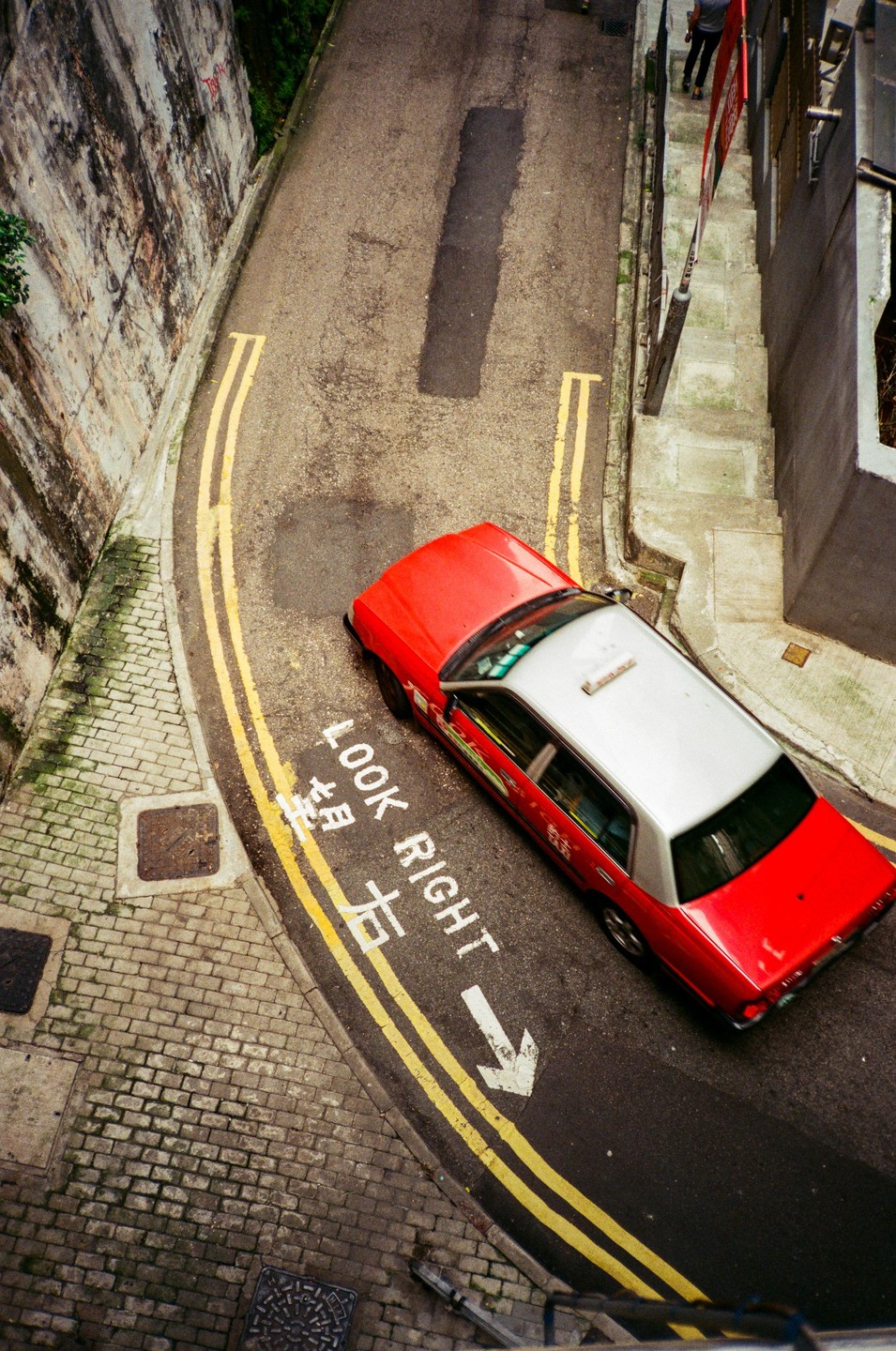 A red and white taxi is parked on a curved street with "LOOK RIGHT" painted on the asphalt.