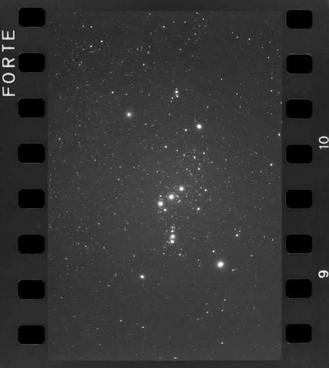A black and white photograph shows a cluster of stars in the night sky.