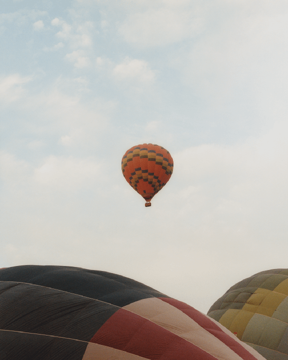 A hot air balloon floats in the sky above other hot air balloons on the ground.