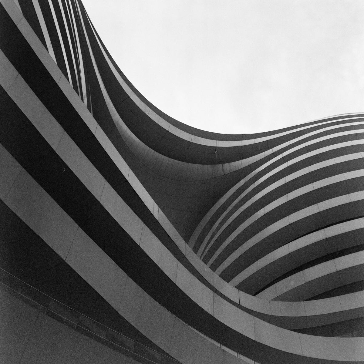 A low-angle view shows the curved, striped facade of a modern building against a bright sky.