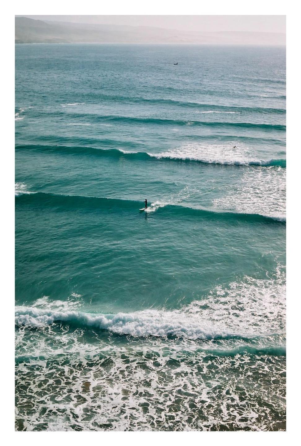 A surfer rides a wave in the ocean with mountains in the distance.