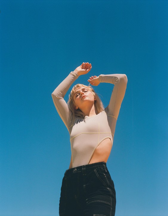 A woman with her arms raised is looking up at a clear blue sky.