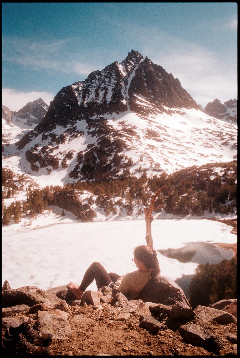 A woman rests on a rock overlooking a frozen lake and snow-covered mountains.