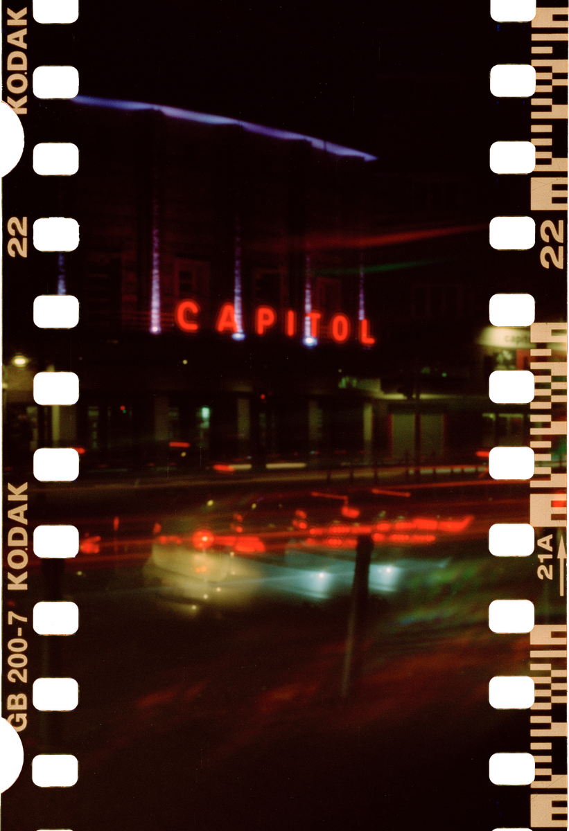 A street at night is illuminated by the neon sign of the Capitol building and the light trails of passing vehicles.