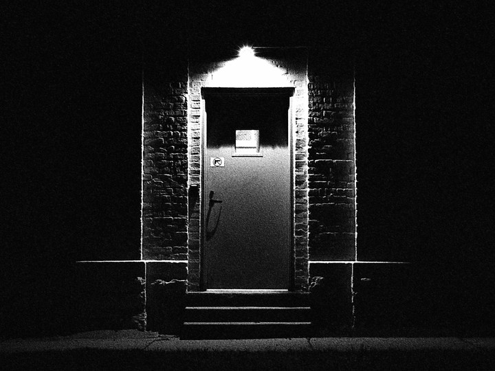 A brightly lit door is centered in a dark brick wall with steps leading up to it.