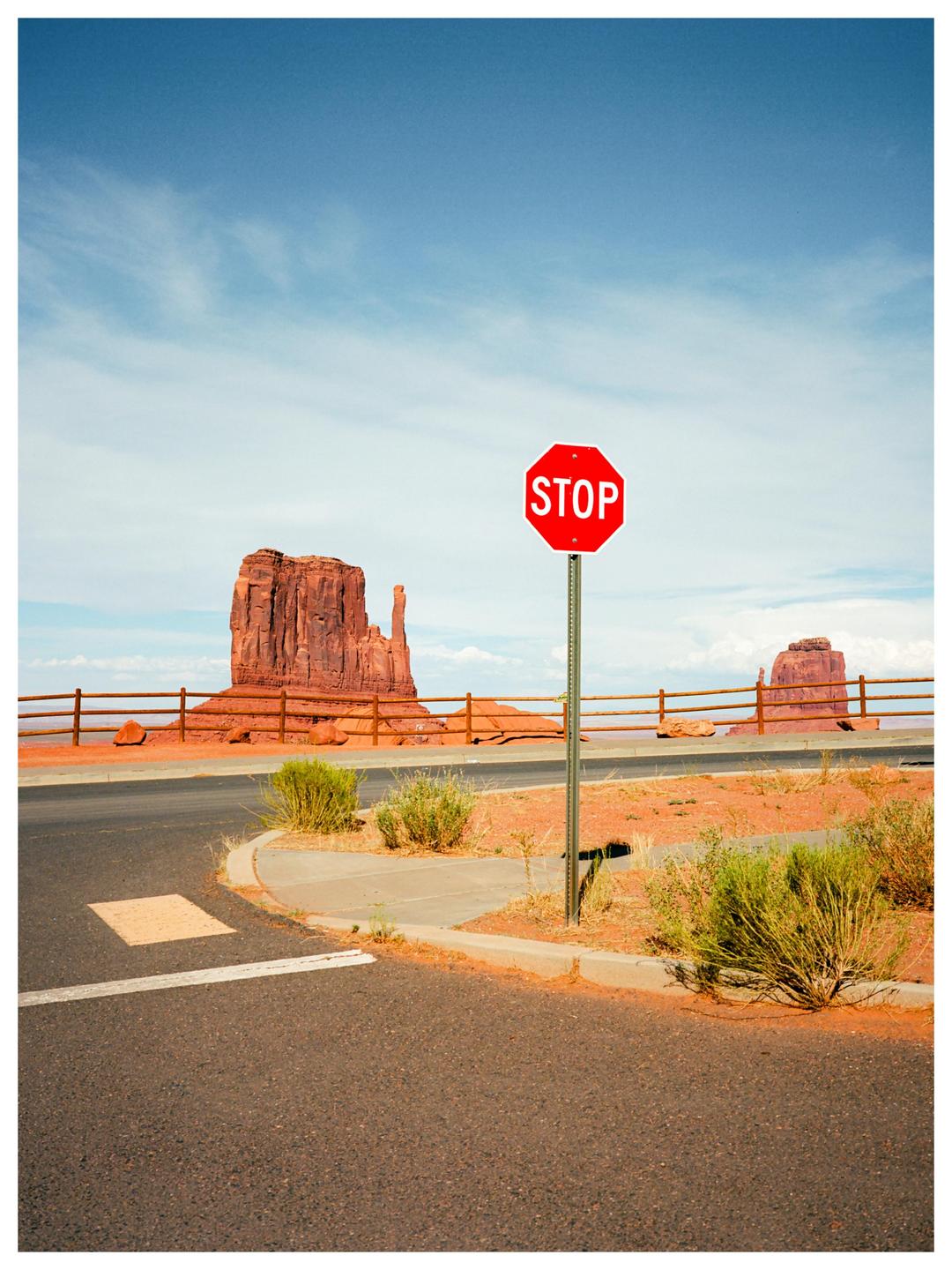 A stop sign stands at a desert intersection with large rock formations in the background.