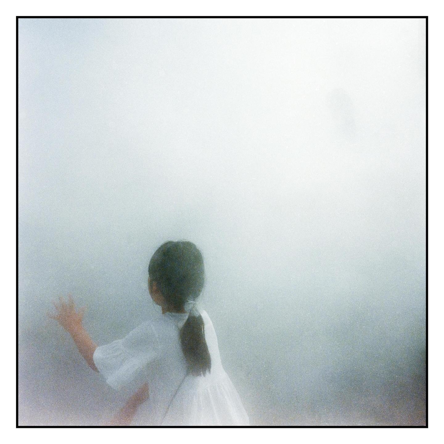 A girl in a white dress with a ponytail reaches out her hand in a hazy, light-filled environment.