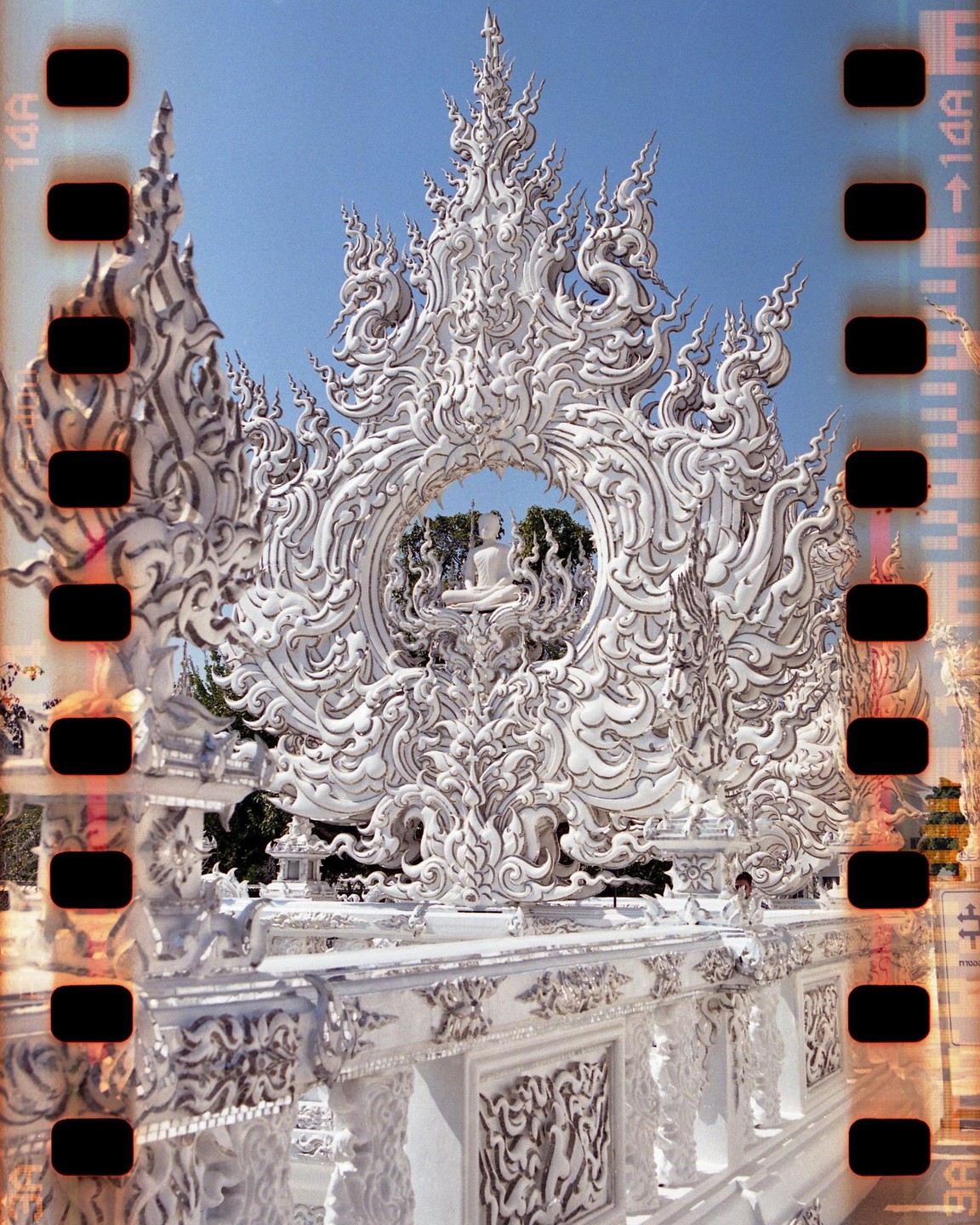 A white ornate temple with a Buddha statue in the center is framed by a clear blue sky.