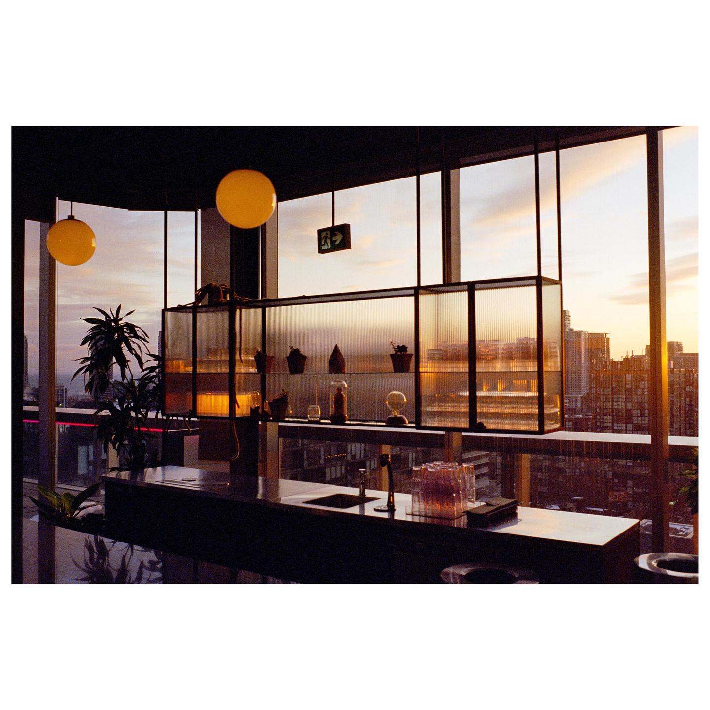 A modern bar area with a cityscape visible through large windows at sunset.