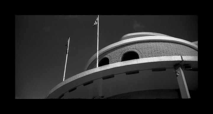 A low-angle view shows a round brick building with arched windows and a flag pole against a dark sky.