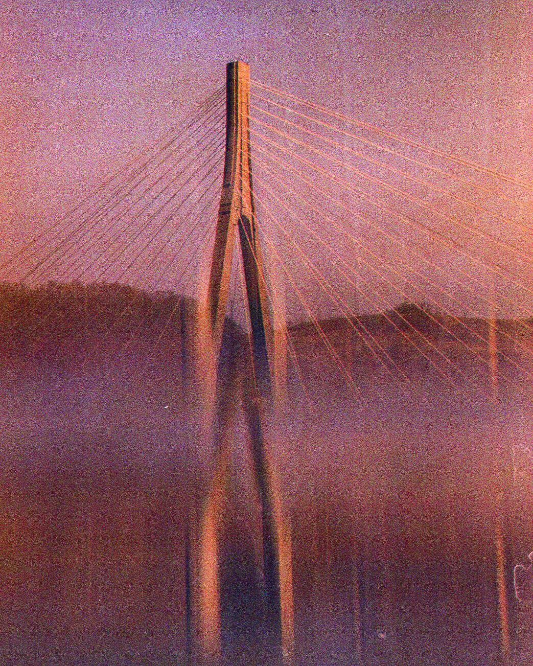 A cable-stayed bridge is visible through a hazy, colorful atmosphere.