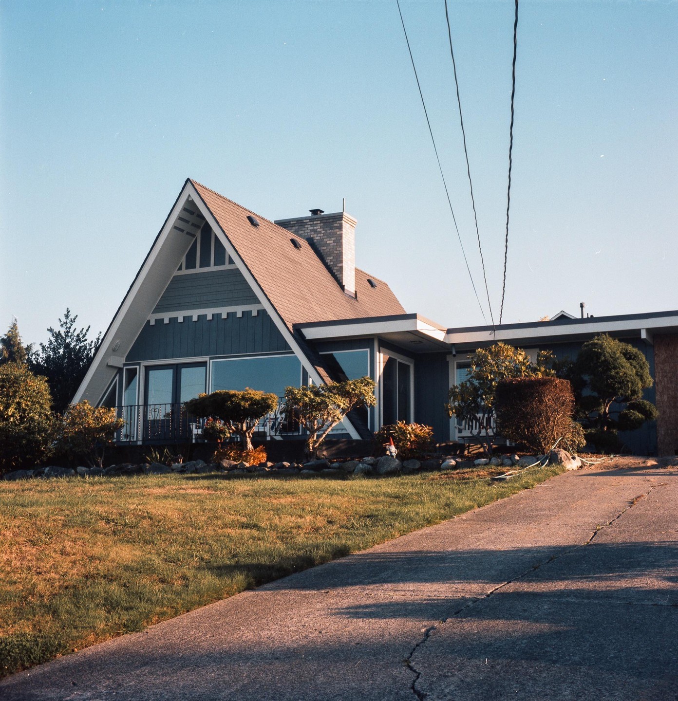 A modern A-frame house with a large front window and a well-maintained lawn is seen from a low angle.