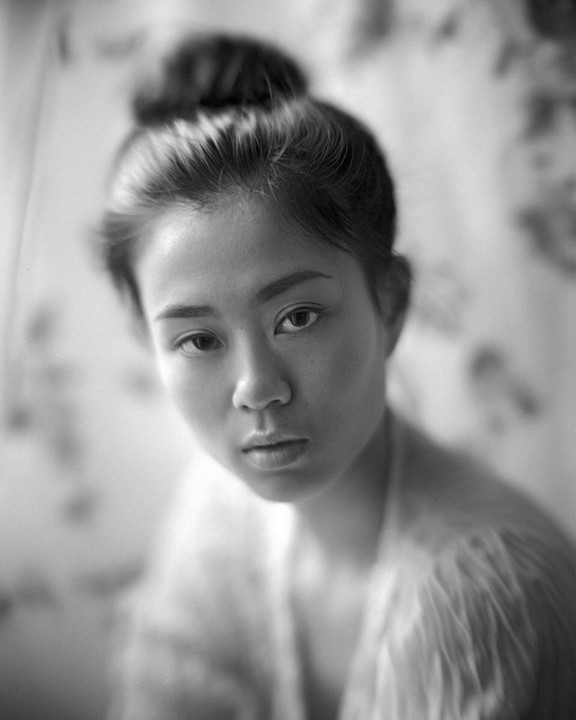 A woman with her hair in a bun looks directly at the viewer.