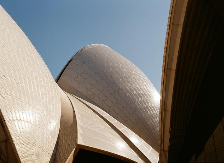 The Sydney Opera House is visible from a low angle, with a clear blue sky in the background.