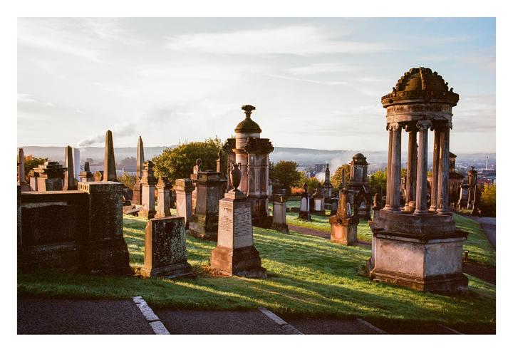 A cemetery with many old gravestones and monuments is visible on a hill overlooking a city.