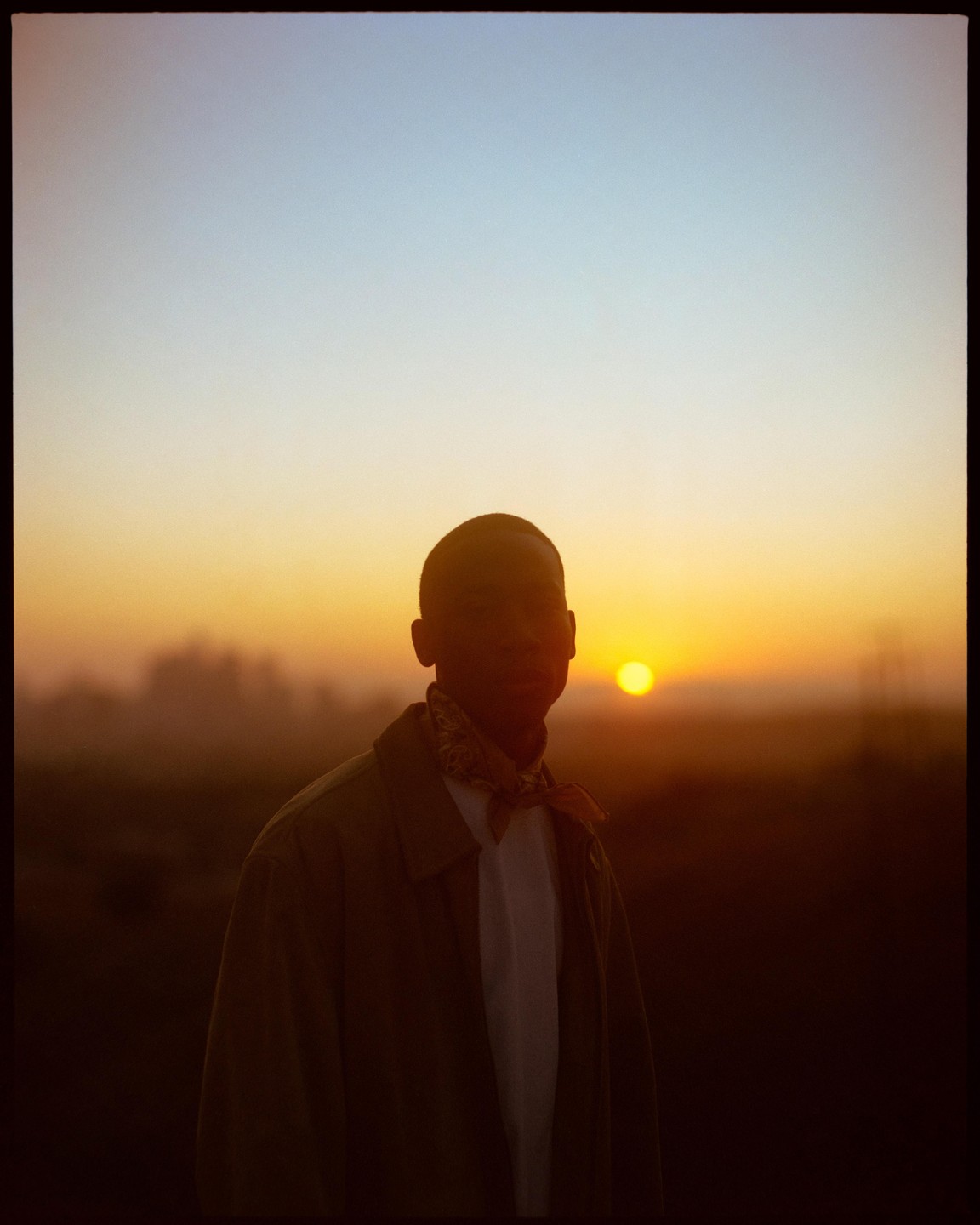 A man stands silhouetted against a vibrant sunset.