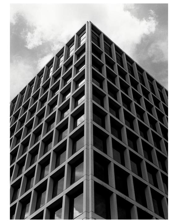 A tall building with a grid pattern of windows is photographed from a low angle against a cloudy sky.