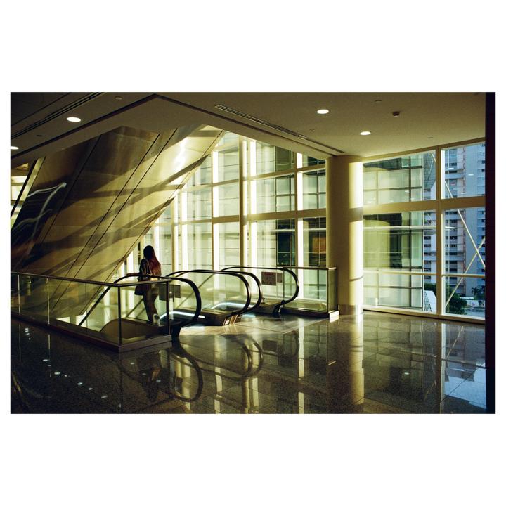 A woman stands on an escalator in a modern building with large windows during golden hour.