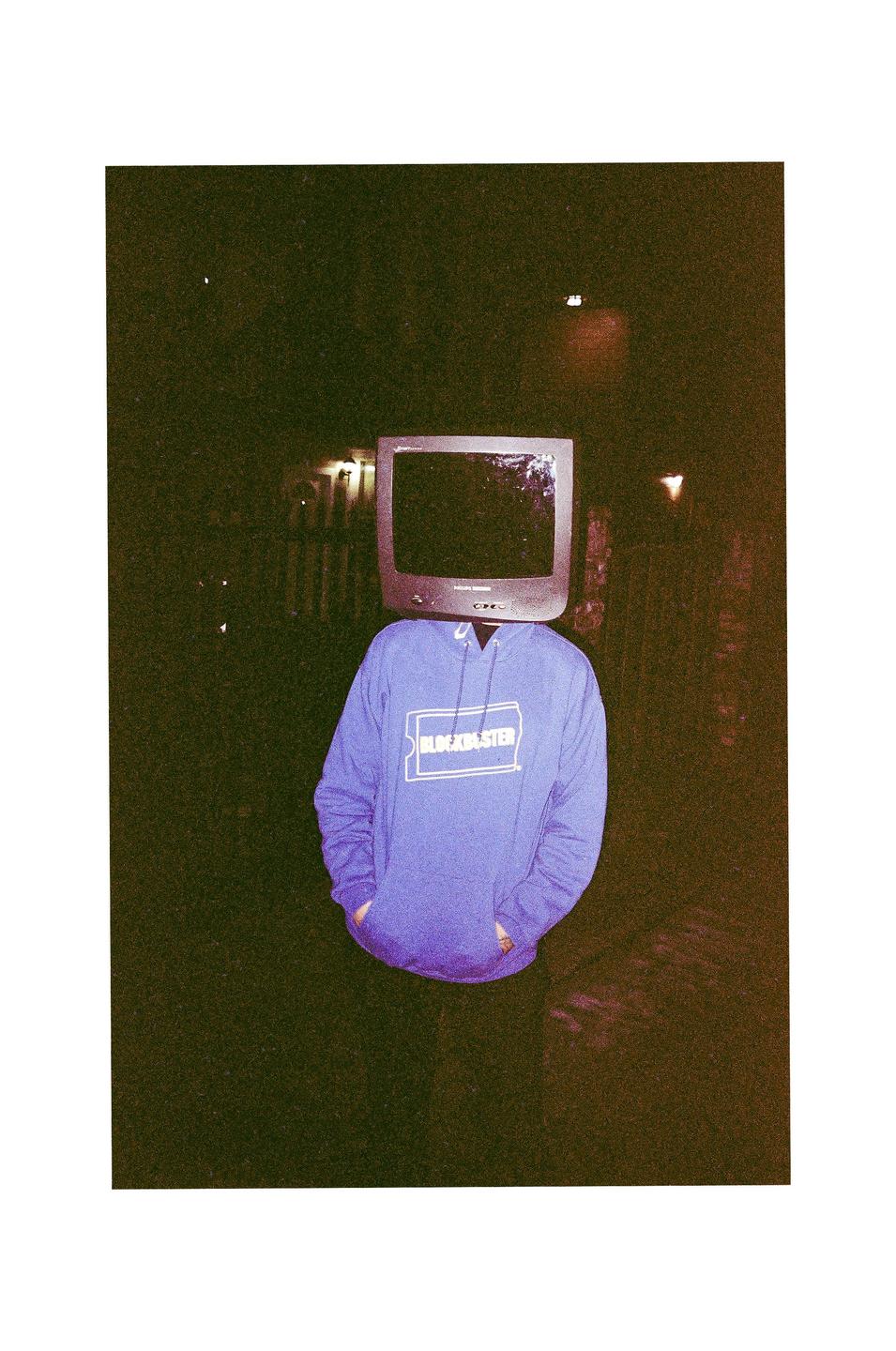 A person wearing a purple Blockbuster hoodie has a television for a head.