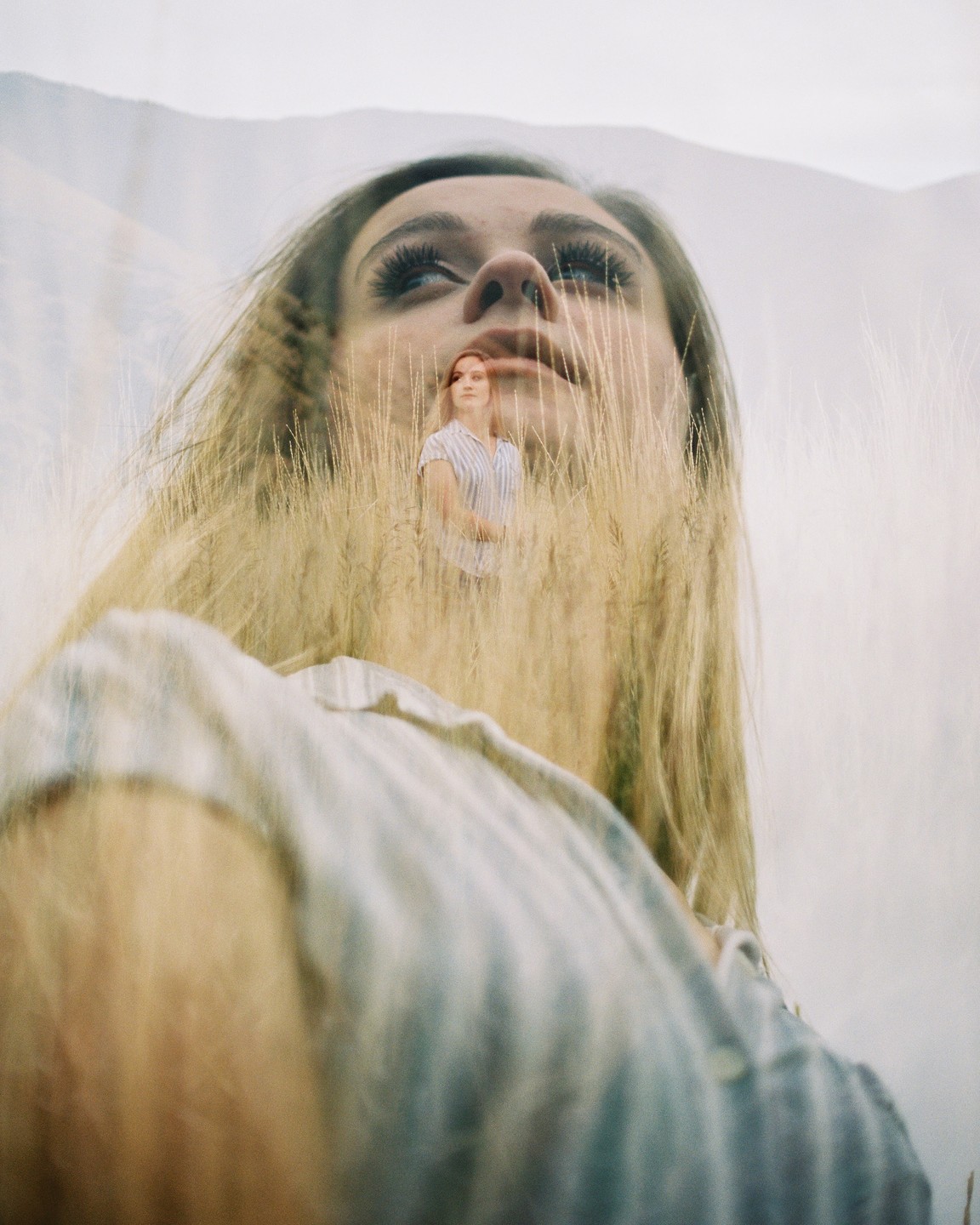 A double exposure shows a woman's face looking up, with a smaller image of a woman standing in a field of wheat superimposed over her face.