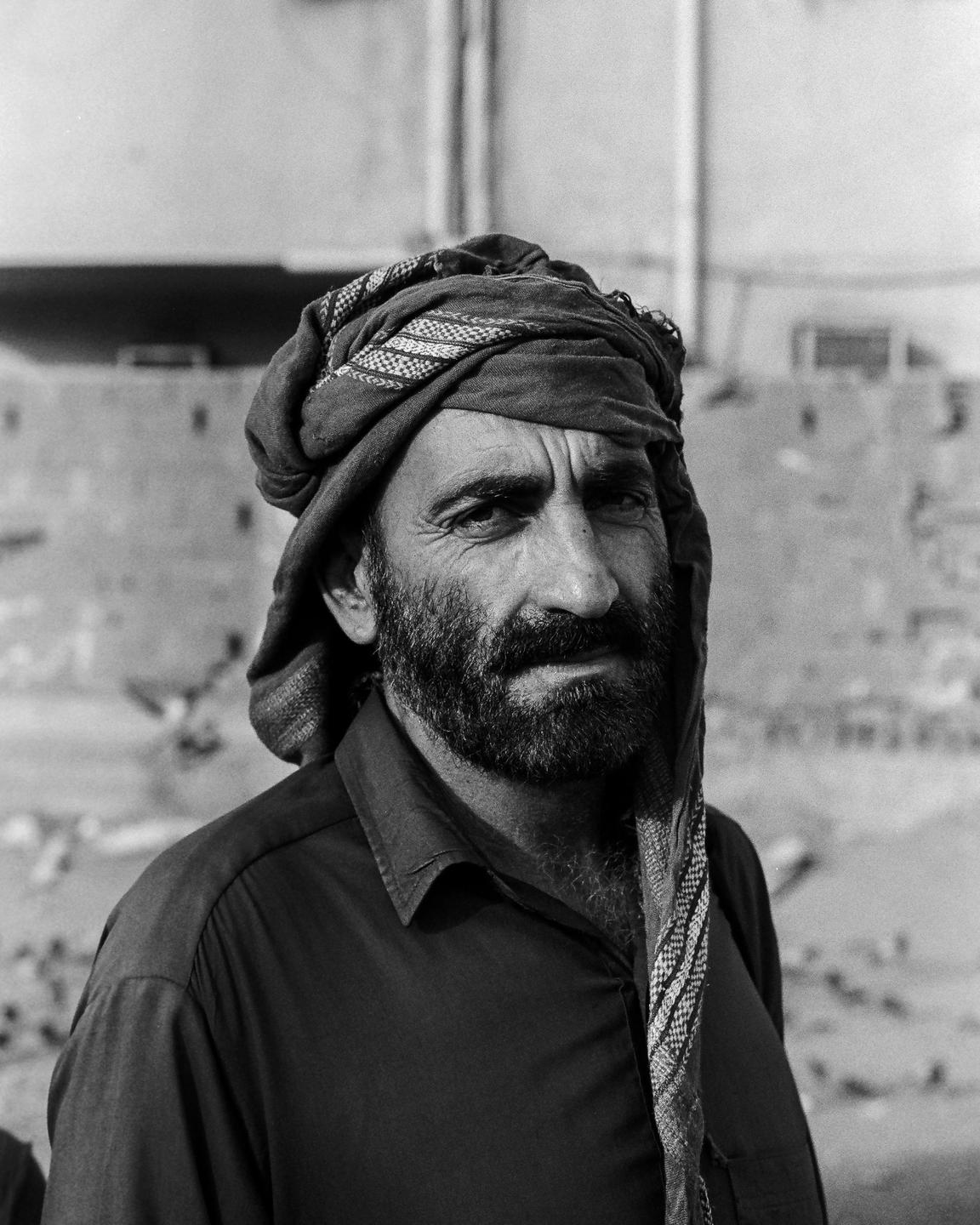 A man with a beard and a patterned turban looks directly at the viewer.