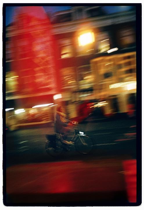 A person rides a moped past blurred buildings at night.