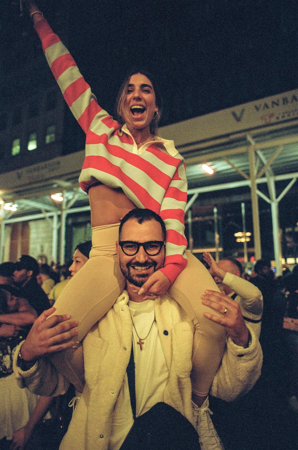 A man carries a woman on his shoulders in a crowd at night.