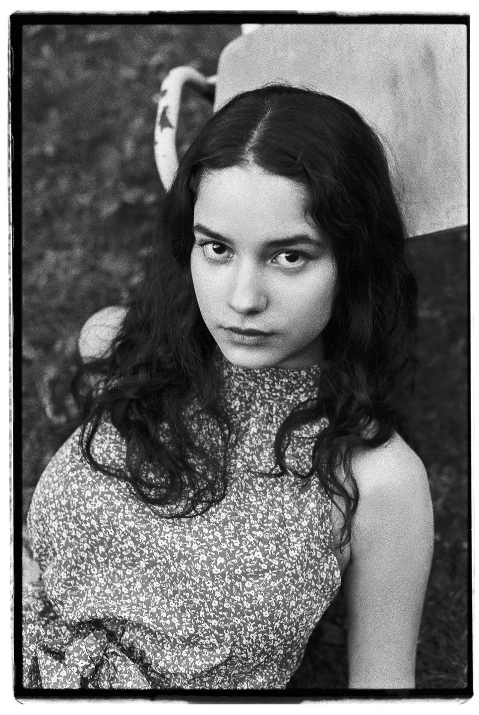 A young woman with long, dark, curly hair looks directly at the viewer.